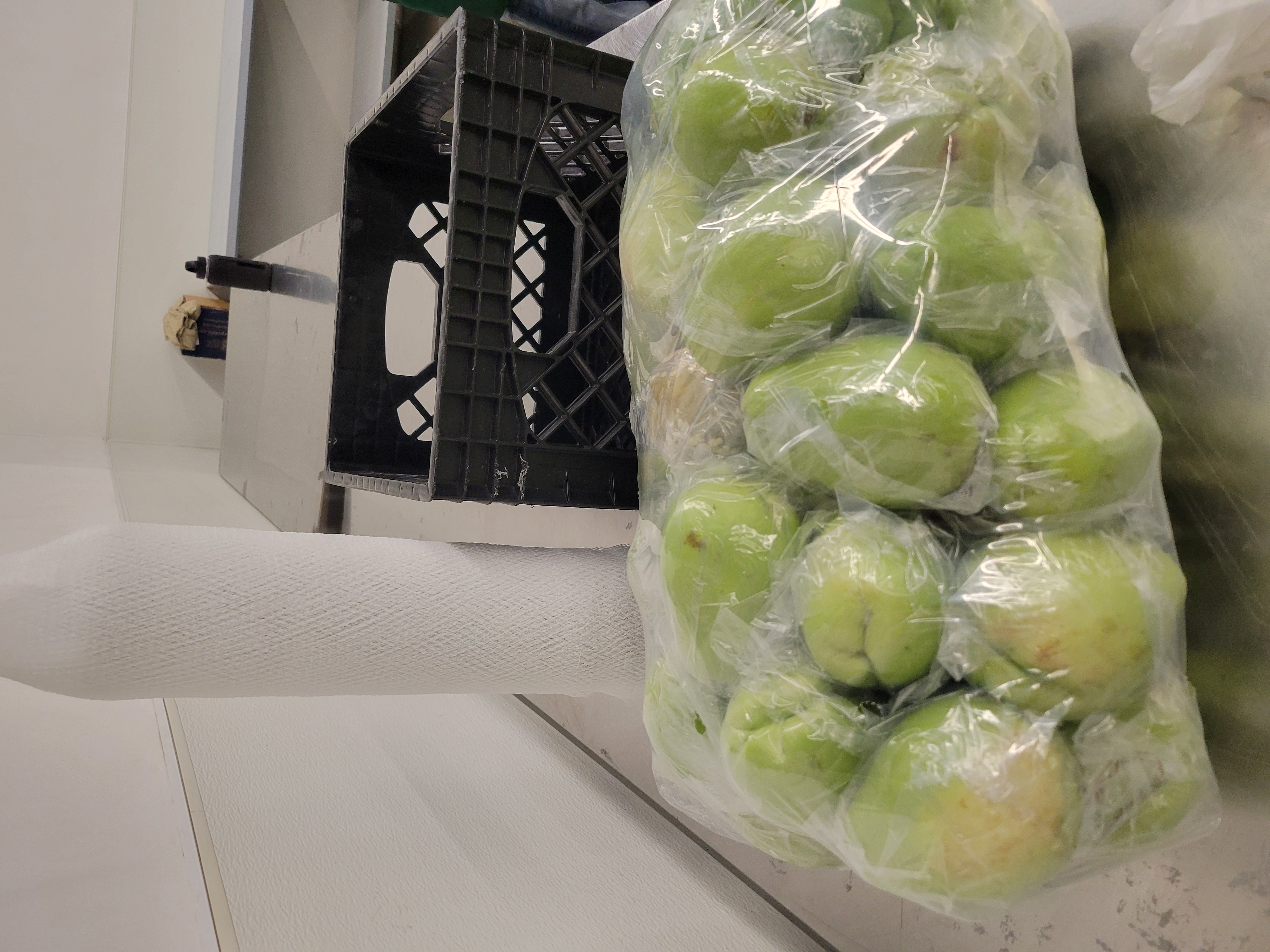 Bag of chayote with crate and bags holder behind it.